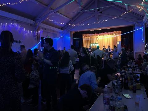 Hall in full swing at 2025 Hogmanay Ceilidh. Lots of people dancing with the Tom Smith Ceilidh Band on stage